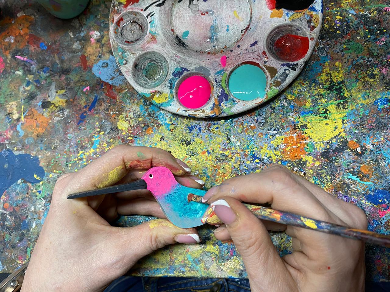 Hands painting a hummingbird mobile.