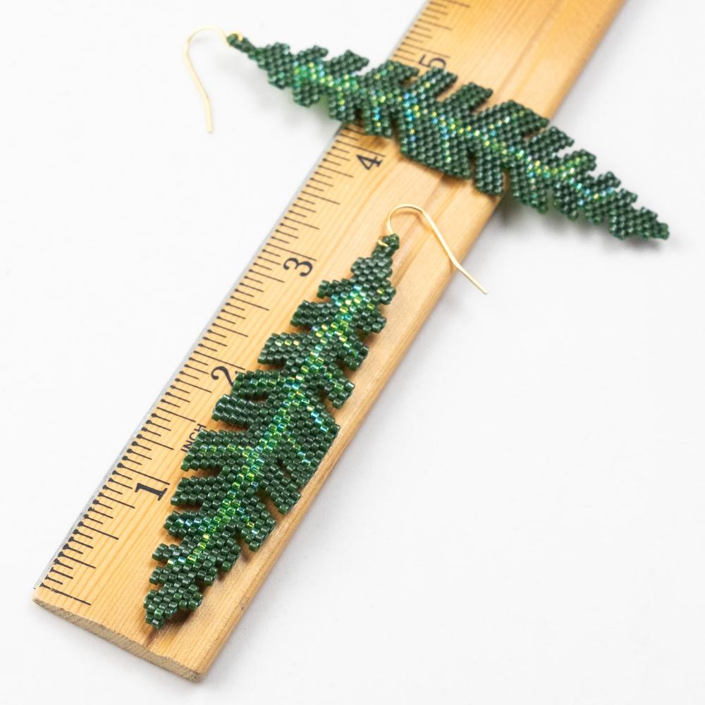 Banana Leaf earrings made of glass beads laying on a wooden ruler