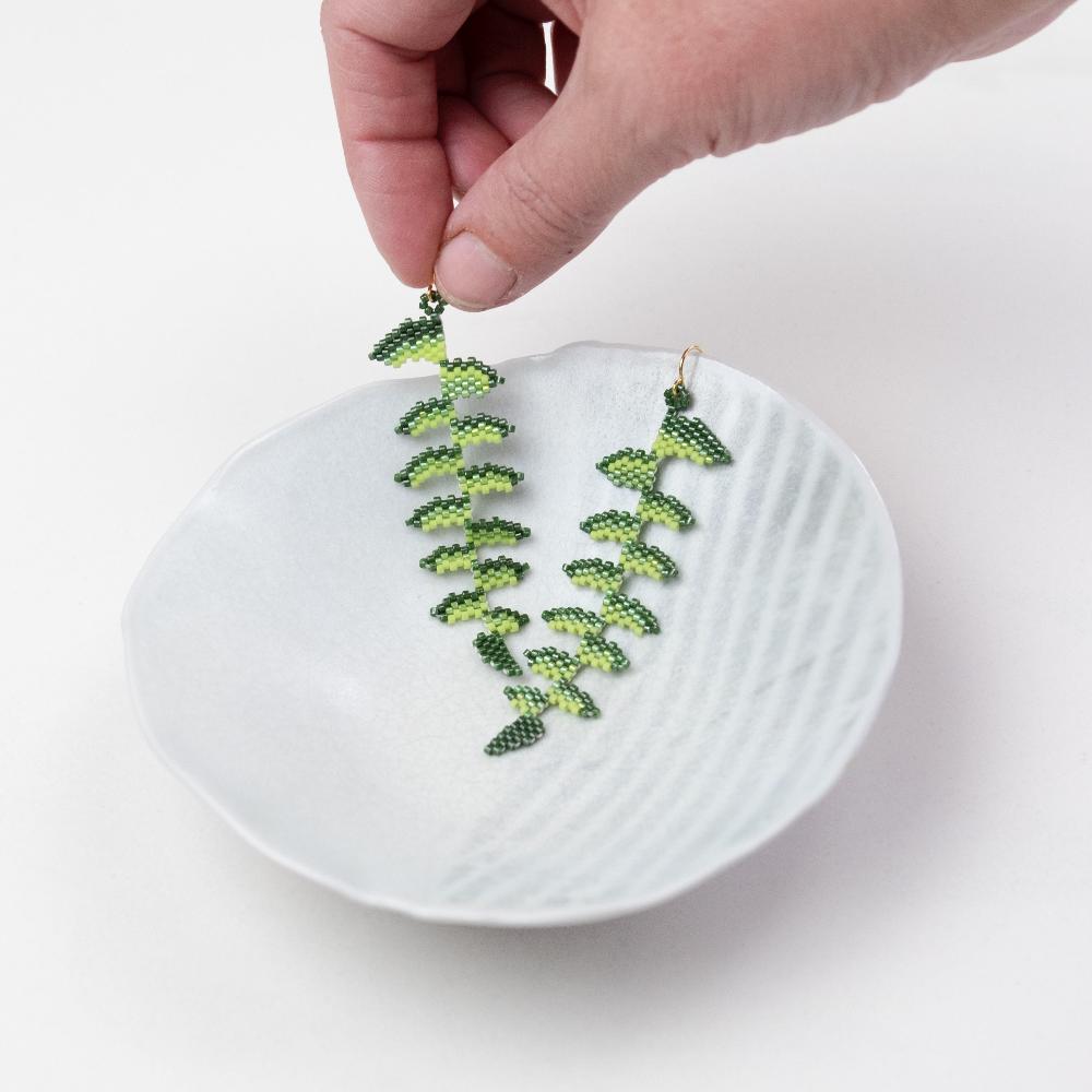 Fern earrings in white ceramic bowl.  Hand model holding up one earring.