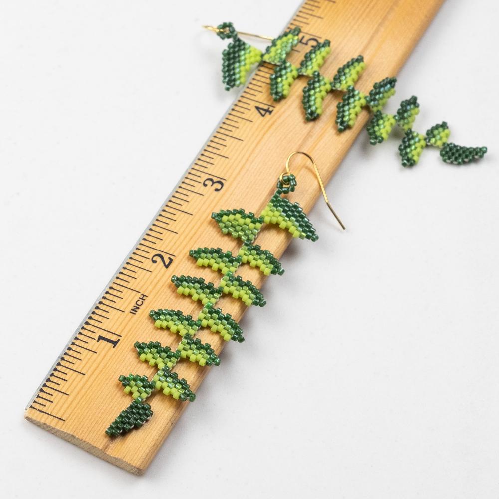 Fern earrings sitting on a wooden ruler.  