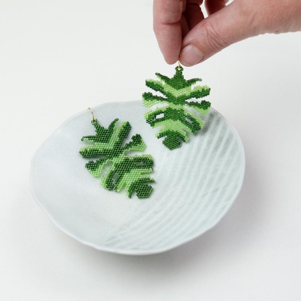 Monstera leaf earrings made of glass beads with hand model and ceramic bowl.